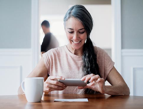 Woman taking photo of check with phone at dining table.