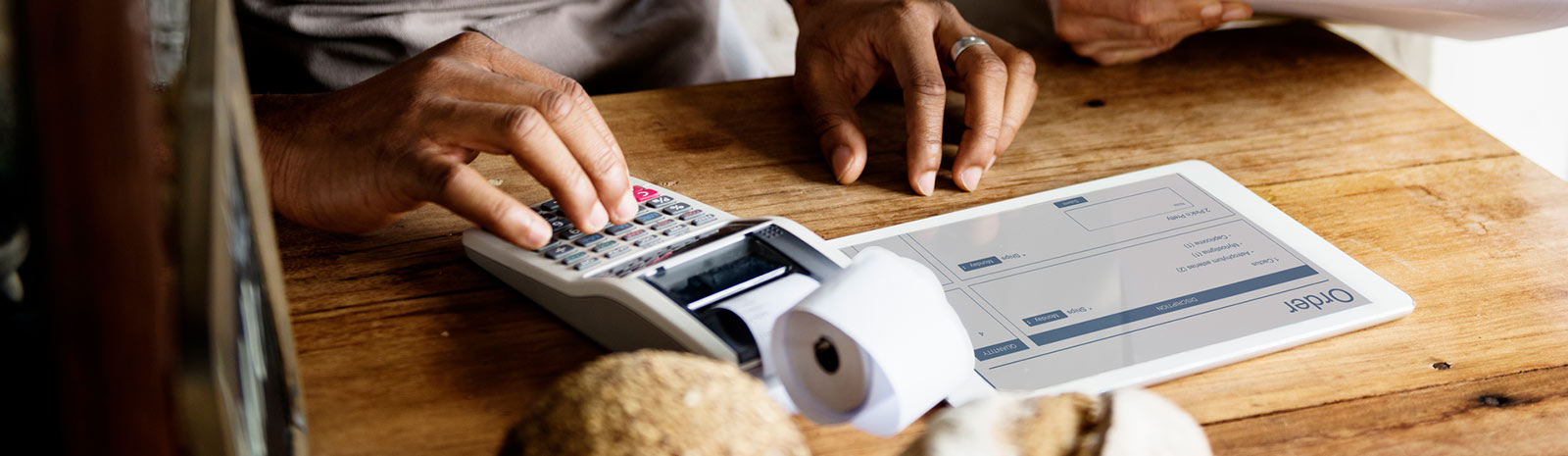 Man typing on adding machine with tablet on table.