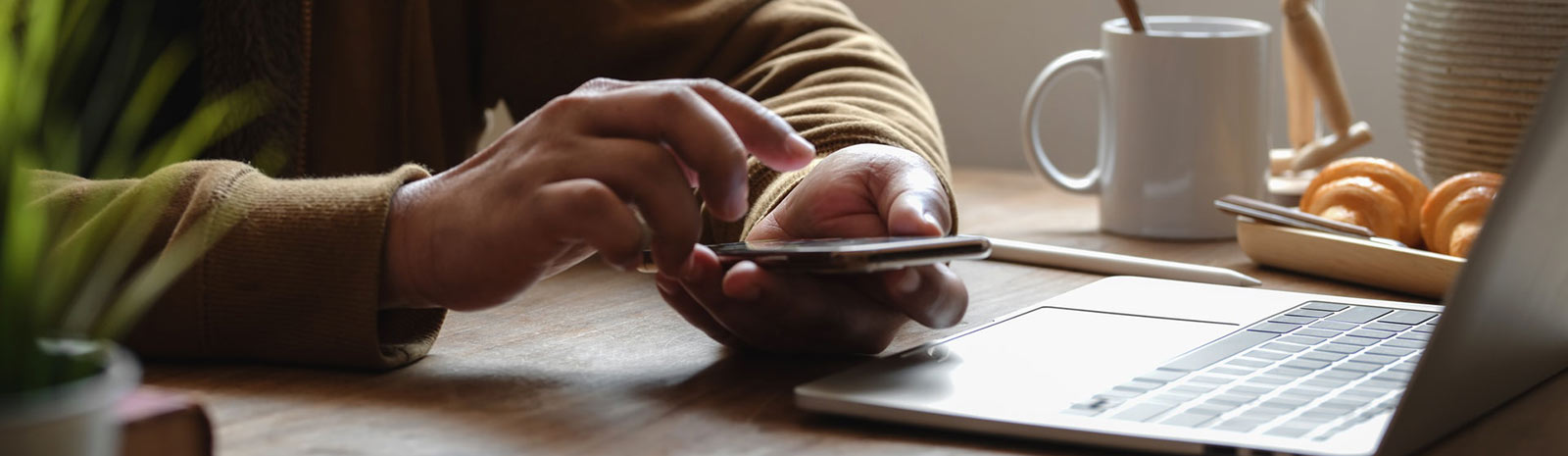 Hands holding phone near laptop.