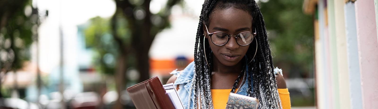 Student holding books looking at phone.